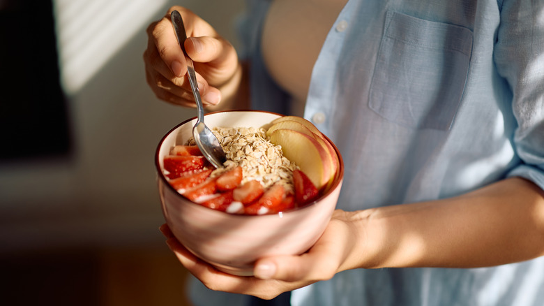 Person eating bowl of oatmeal with strawberries on top