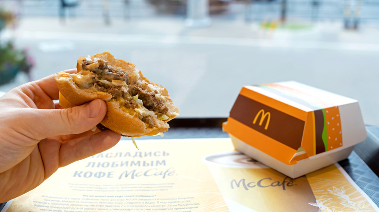 Person holding a McDonald's Big Mac with bites taken from it next to the cardboard Big Mac box.