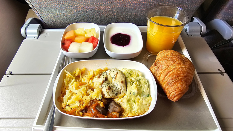 Breakfast food including croissant, fruit, and orange juice on an airplane tray table