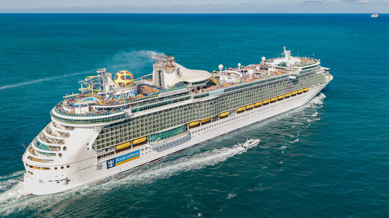 A white cruise ship full of people moving through the blue ocean with pale blue sky in the background
