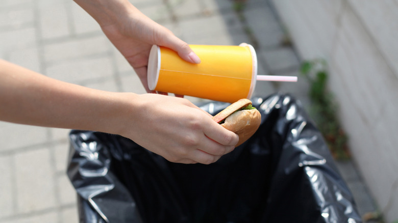 Hands throwing away a drink container and a hot dog