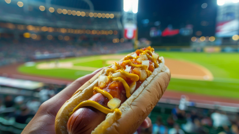 Hot dog with toppings in front of a baseball stadium diamond