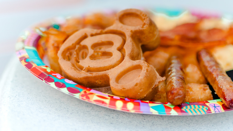 Mickey Mouse pancakes with sausage and bacon on a paper plate