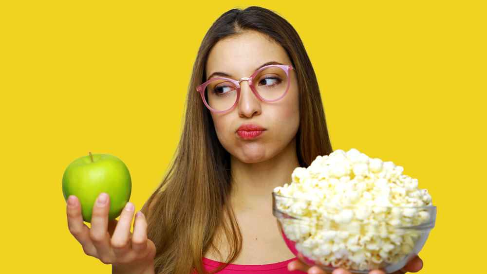 Woman choosing between apple and popcorn