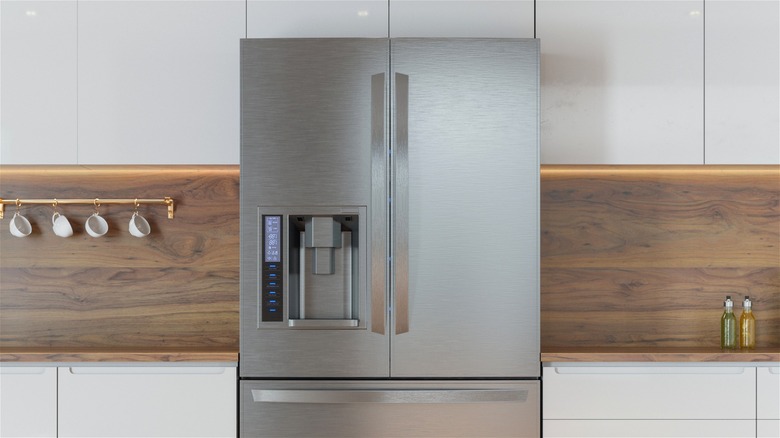 Chrome refrigerator with water dispenser and external control panel in modern kitchen.
