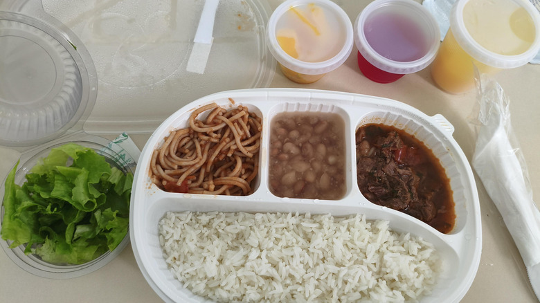 Portioned Brazilian hospital food of lettuce, noodles, beans, meat, rice, and liquid cups.