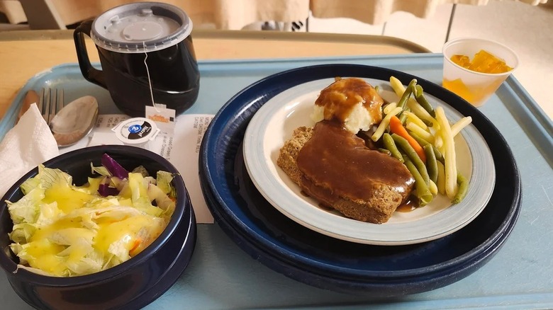 Hospital tray with hot tea, salad with dressing, plate of meatloaf and veggies, and Jell-O cup.