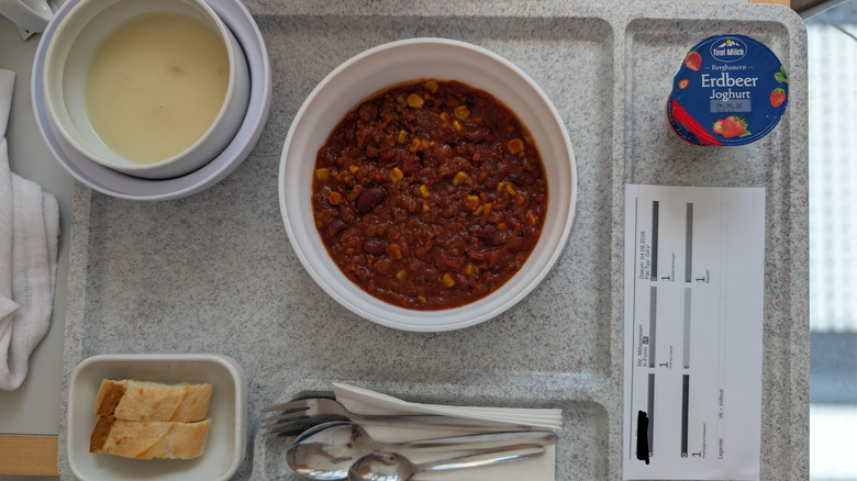 Hospital tray with asparagus soup, bread, chili con carne, and strawberry yogurt.