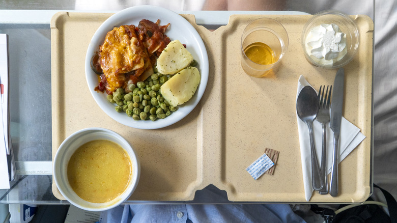 Tray of hospital food consisting of meat, peas, potatoes, and broth.
