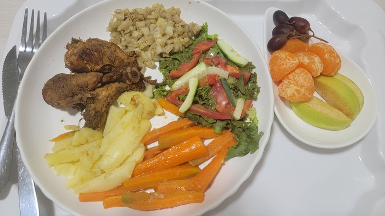 Grilled chicken, boiled carrots and potatoes, and salad with fruit on the side.