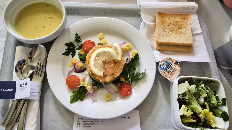 Hospital tray with curry soup, green salad, salmon tartare, diced avocado, and toast.