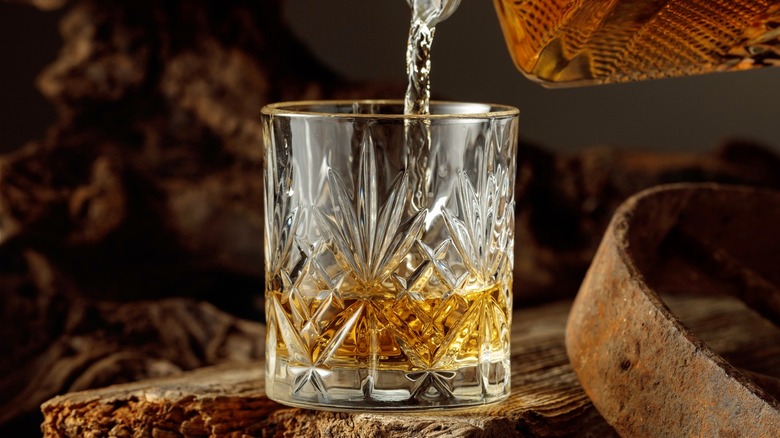 Whiskey being poured from a decanter into a glass, set against a rustic backdrop.