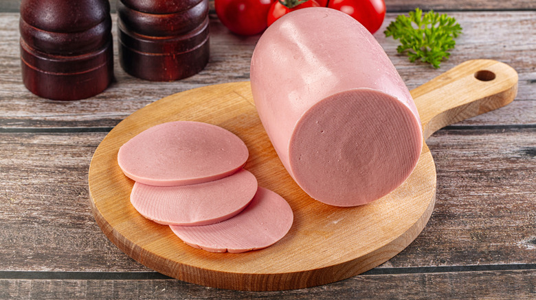 Bologna on cutting board with salt and pepper grinders, tomatoes, garlic, and parsley in the background
