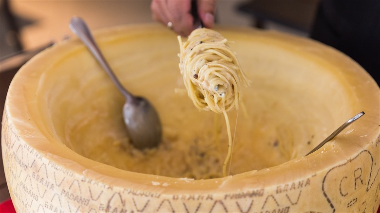 Person twirling pasta over cheese wheel
