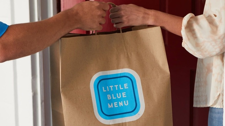 Delivery person handing Little Blue Menu bag to customer.