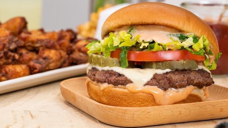 Little Blue Menu burger on wooden tray in front of chicken wing platter.