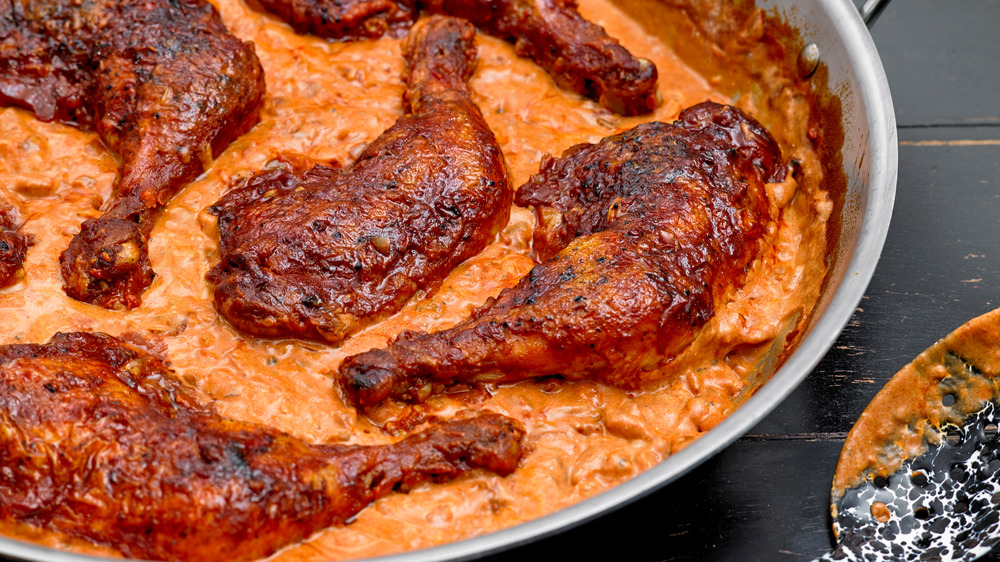 Chicken legs and thighs with creamy orange-colored paprikash sauce in a pan.