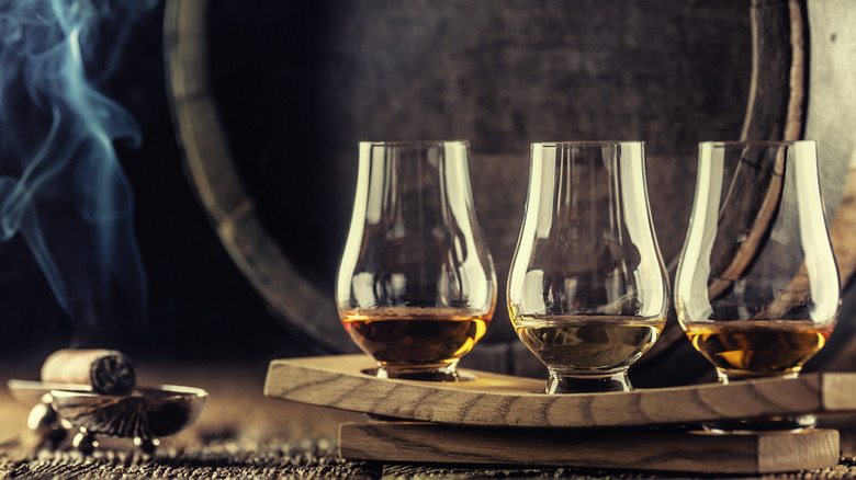Smoking cigar beside whiskey glasses and cask