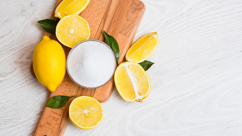 Citric acid powder surrounded by lemons on wooden board