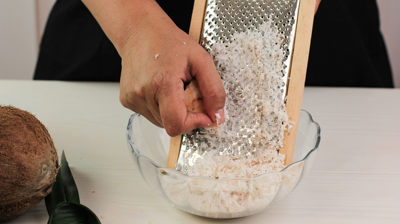 Person grating coconut into glass bowl