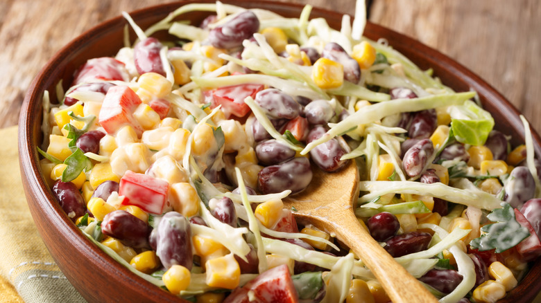 Brown bowl and spoon with dressed cabbage, peppers, beans, corn, cilantro