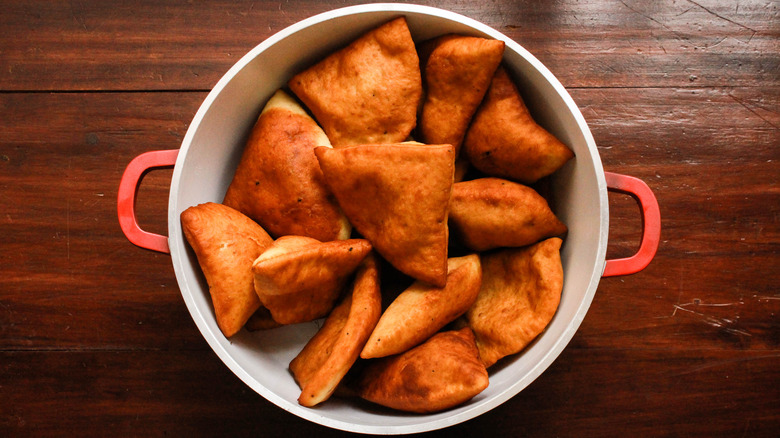 Red handled pot full of mandazi on wood table