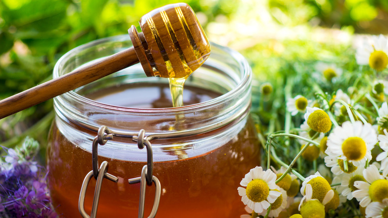 Jar of honey with honey spool and flowers