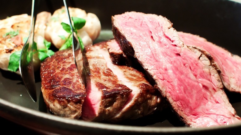Ribeye cap steak with tongs and herbs