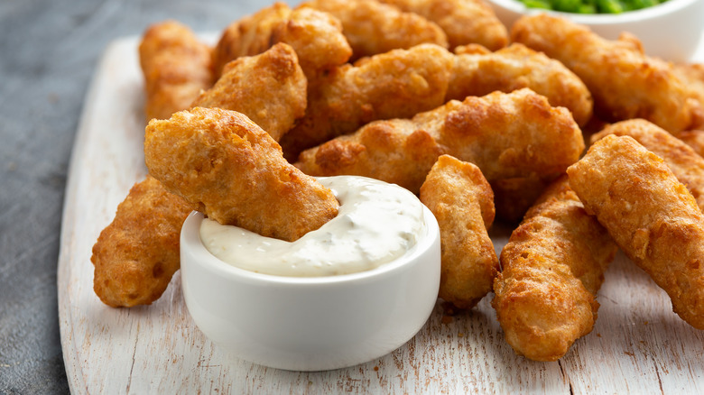 Assortment of small fish filets with one dipped in a bowl of tartar sauce