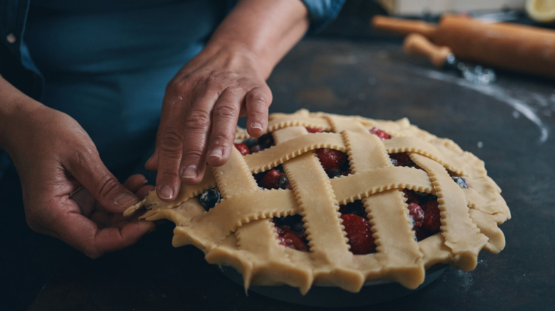 Hands crimping edges of lattice crust on berry pie.