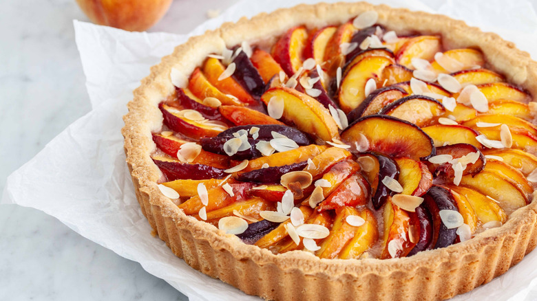 Peach tart with almond topping on white paper.