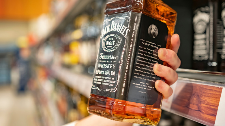 Hand holding Jack Daniel's bottle in front of store shelf.