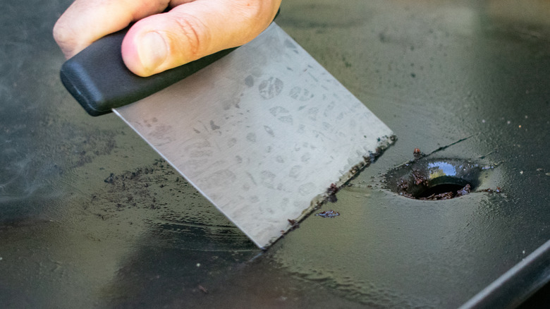 Closeup of a person using a board scraper to clean the surface of a flat-top griddle