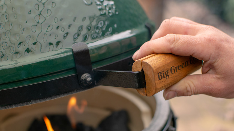 Hand holding handle to open Big Green Egg grill