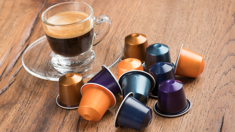 Espresso in a clear small cup and saucer next to colorful Nespresso pods