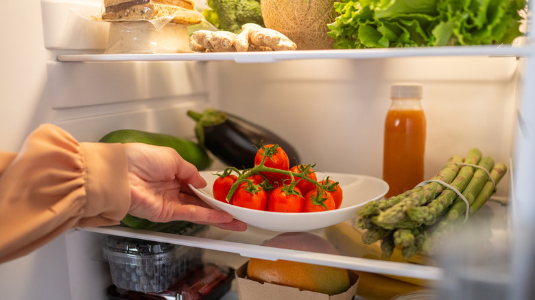 Plate of vine tomatoes in fridge alongside other produce