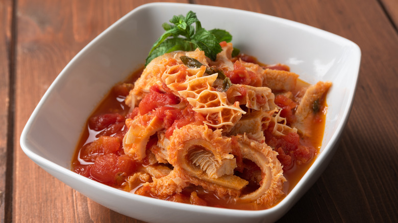 A white bowl of stewed tripe and tomatoes with basil on top