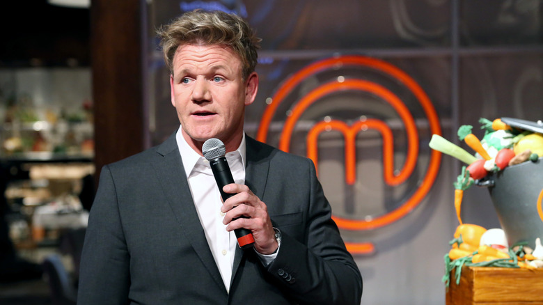 Gordon Ramsay talking into microphone in front of MasterChef logo