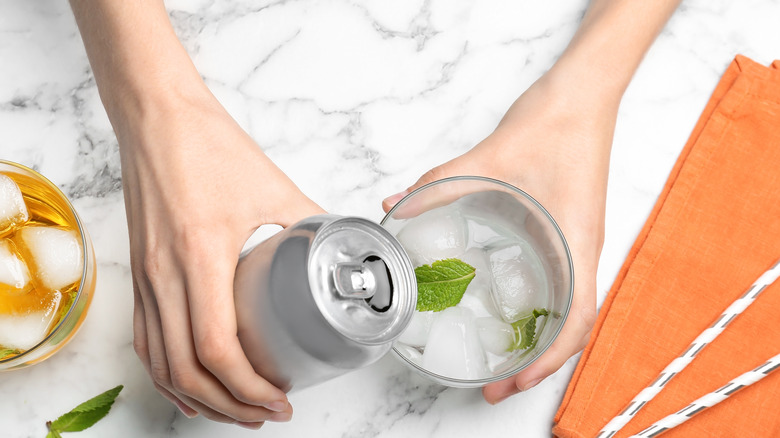 pouring a canned drink into a glass of ice