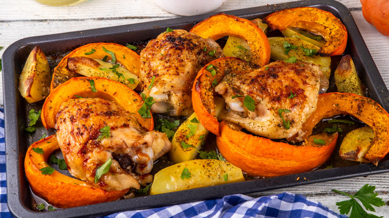 Roast chicken thighs with potatoes and squash on baking tray