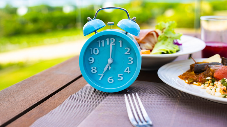 Alarm clock with plates of food and fork on table outside