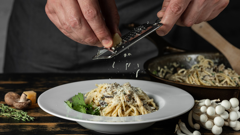 Shaving cheese over a bowl of pasta