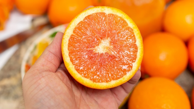 Hand holding one half of a cara cara orange with the flesh exposed ad oranges in the background