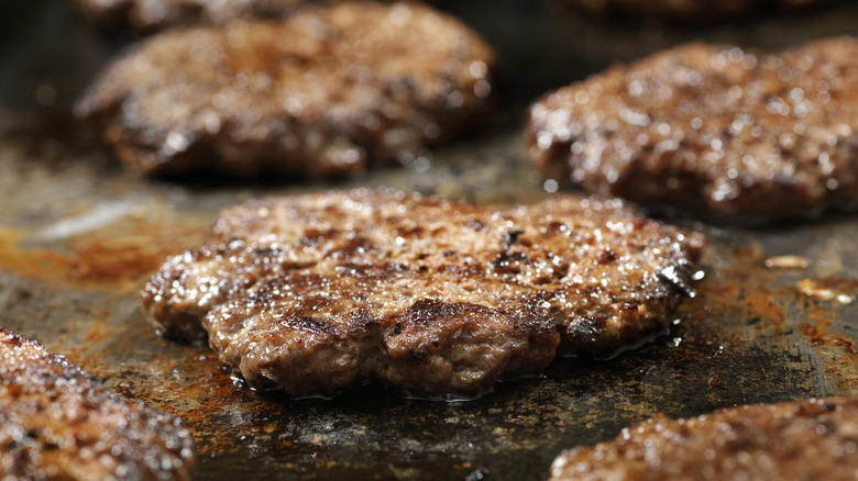 Burger patties cook on a griddle.