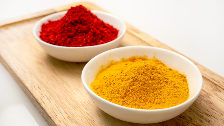 Paprika and turmeric powder in white bowls on top of a wooden serving tray