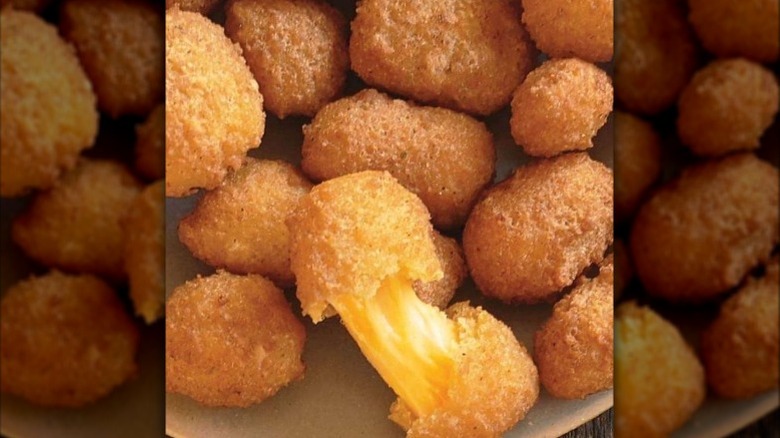 A pile of Culver's cheese curds with one curd pulled apart to show cheese pull