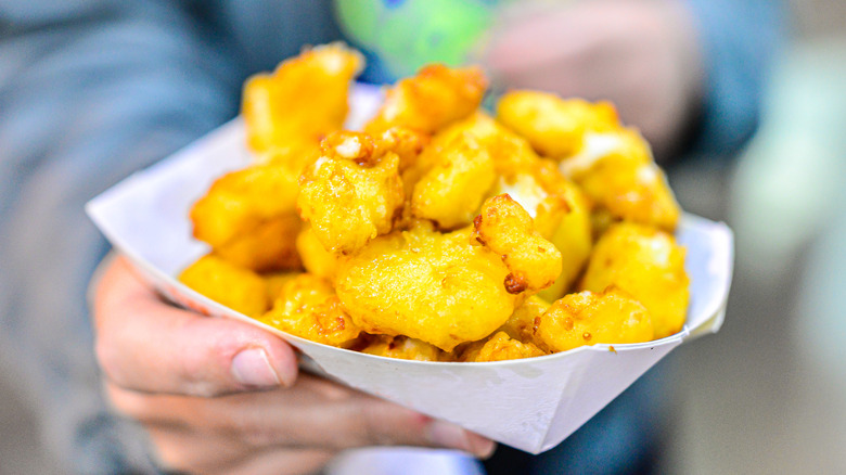 A hand holding cheese curds in a paper plate