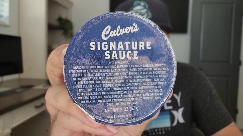 A hand holding up a Culver's Signature Sauce takeaway cup close to the camera