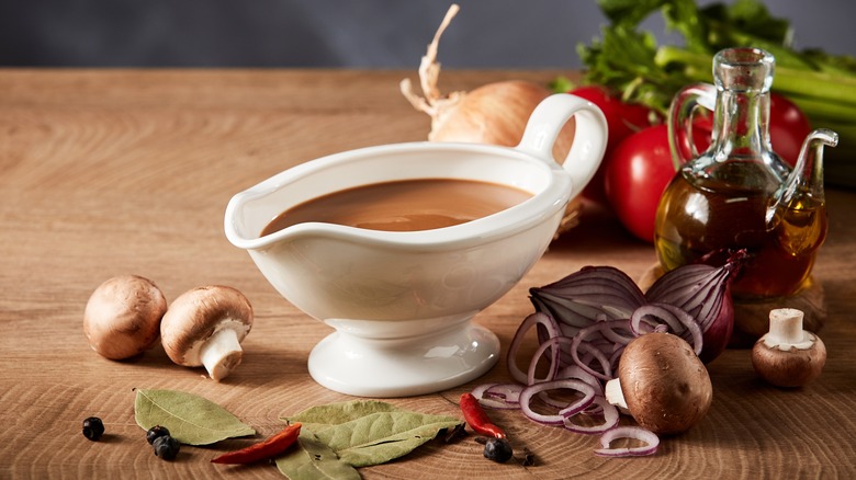 A pot of gravy next to vegetables, oil and herbs