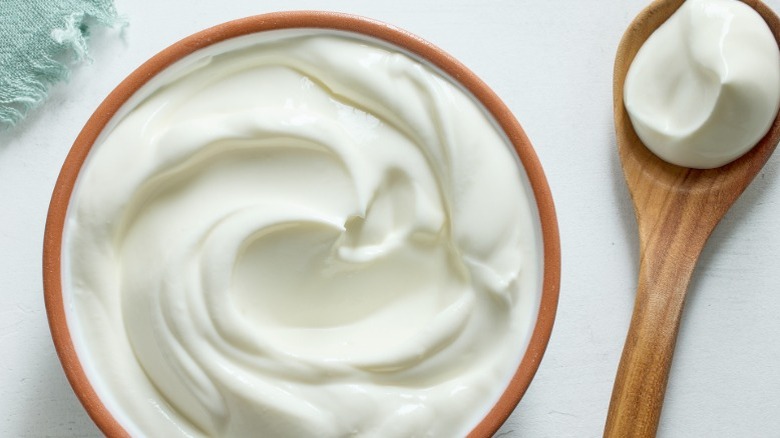 Bowl of sour cream next to a wooden spoon with sour cream in it
